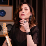 A cantora Pitty segurando uma guitarra em estúdio, diante de caixas amplificadoras